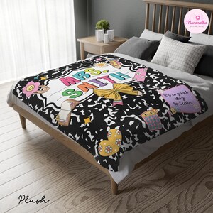 May include: A plush blanket with a black and white design featuring the text "MRS SMITH" in colorful letters. The blanket has a school-themed design with flowers, a bow, and the phrase "It's a good day to learn."