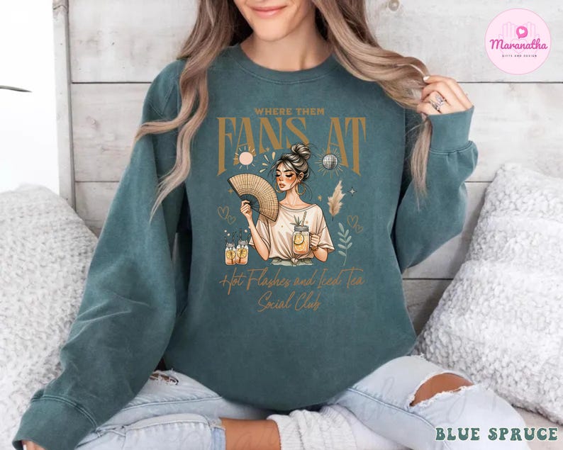 Puede incluir: Una sudadera azul turquesa con un dise&ntilde;o gr&aacute;fico que presenta a una mujer sosteniendo un abanico y un vaso de t&eacute; helado. El texto en la sudadera dice "Where them fans at Hot Flashes and Iced Tea Social Club".