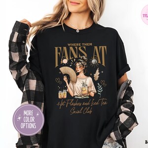 Puede incluir: Camiseta negra con un gr&aacute;fico de una mujer sosteniendo un abanico y un vaso de t&eacute; helado. El texto "Where Them Fans At" est&aacute; por encima del gr&aacute;fico y "Hot Flashes and Iced Tea Social Club" est&aacute; por debajo del gr&aacute;fico.