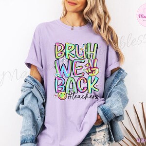 K&ouml;nnte beinhalten: Ein helllila T-Shirt mit den Worten "BRUH WE BACK" in einem farbenfrohen Graffiti-Design. Das Shirt zeigt auch ein Friedenszeichen und den Hashtag #teachers.