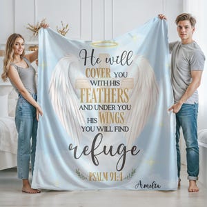 May include: A blue and white throw blanket with a religious quote and a white angel wing design. The quote reads "He will cover you with his feathers and under you his wings you will find refuge Psalm 91:4 Amelia".