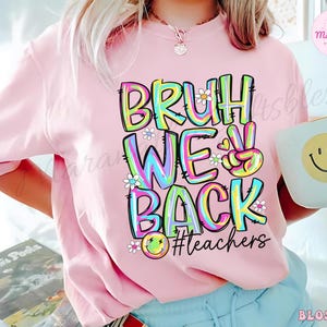 K&ouml;nnte beinhalten: Hellrosa T-Shirt mit dem Text "BRUH WE BACK #teachers" in einem farbenfrohen, im Batik-Stil gehaltenen Schriftzug. Das Design beinhaltet G&auml;nsebl&uuml;mchen und ein Smiley. Das Shirt hat eine l&auml;ssige, &uuml;bergro&szlig;e Passform.