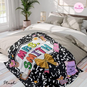 May include: A plush blanket with a black composition notebook design and the name "MRS SMITH" in colorful letters. The blanket features a yellow bow, a pencil, and the text "It's a good day to learn."