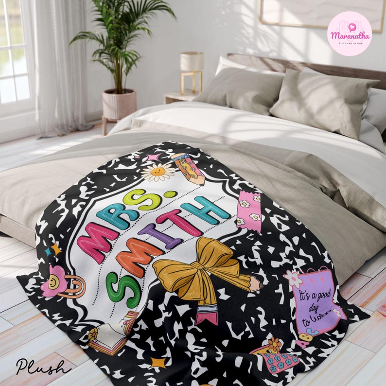 May include: A plush blanket with a black composition notebook design and the name "MRS SMITH" in colorful letters. The blanket features a yellow bow, a pencil, and the text "It's a good day to learn."