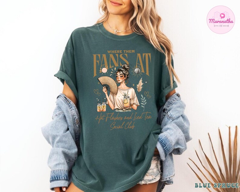Puede incluir: Una camiseta azul turquesa con un dise&ntilde;o gr&aacute;fico que presenta a una mujer con un abanico, el texto "Where Them Fans At" y las palabras "Hot Flashes and Iced Tea Social Club".