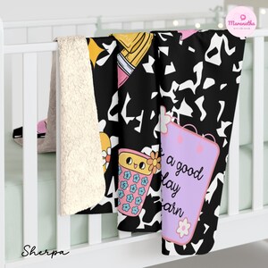 May include: A black and white patterned blanket with a sherpa lining. The blanket features cartoon graphics of a calculator, pencils, and a notepad with the text "a good day to learn". The blanket is draped over a white crib.