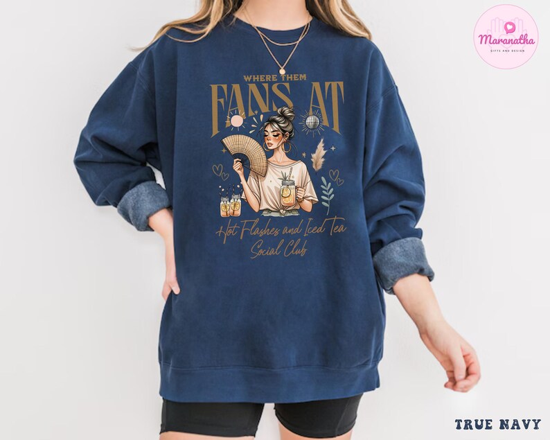 Puede incluir: Una sudadera azul marino con un gr&aacute;fico de una mujer sosteniendo un abanico y un vaso de t&eacute; helado. El texto "Where Them Fans At" est&aacute; por encima del gr&aacute;fico, y el texto "Hot Flashes and Iced Tea Social Club" est&aacute; por debajo del gr&aacute;fico.