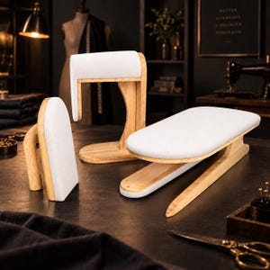 May include: A set of three wooden tailoring tools with white fabric padding, including a vertical sleeve board, a curved pressing ham, and a long, flat ironing board. These sewing accessories feature light-toned wood bases and smooth, padded surfaces.
