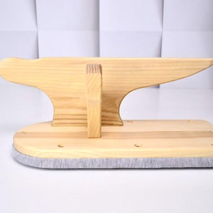 May include: A wooden tailor's clapper, a pressing tool used in sewing. The clapper is made of light-colored wood and has a rectangular base with a gray fabric edge. The top is shaped like an anvil.