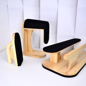 May include: A set of three wooden tailoring tools featuring light-colored natural wood bases and upright supports topped with smooth black fabric padding. The collection includes a vertical press, a curved sleeve board, and a flat pressing board.