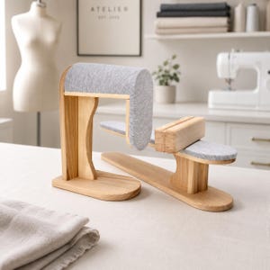 May include: A wooden tailor's ham and sleeve board set featuring light-toned wood bases and grey fabric-covered pressing surfaces. The taller unit has a curved, padded top, while the lower unit includes a flat, rectangular wooden block.