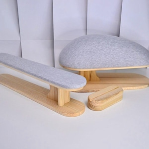 Könnte beinhalten: Ein Set aus Holz-Schneiderwerkzeugen, darunter ein langes Bügelbrett, ein abgerundetes Bügelbrett und ein kleines Schneiderkissen. Die Bretter haben hellgraue gepolsterte Oberflächen und stehen auf Naturholzsockeln.