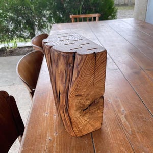 Pode incluir: Um bloco de facas de madeira r&uacute;stico com ranhuras para segurar as facas. O bloco &eacute; feito de uma pe&ccedil;a grossa de madeira com um acabamento natural toscamente talhado. Tem uma cor castanho escuro e uma forma ligeiramente curva.