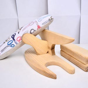 Può includere: Un set di strumenti di cucito in legno, tra cui un asse per maniche, un cuscinetto per stiratura e un clapper. L'asse per maniche è rivestito in tessuto bianco stampato con forbici colorate. Gli altri strumenti sono in legno chiaro.