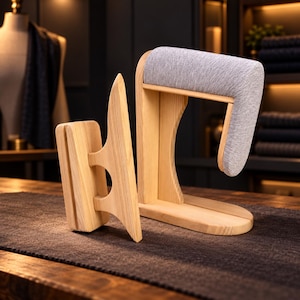 Op de afbeelding: Een lichtgekleurde houten kleermakersklos en een houten mouwstrijkplank met een grijze stoffen bekleding. De klos is een rechthoekig blok met een handvat, terwijl de mouwplank een gebogen, gevoerde arm heeft voor het strijken van kleding.
