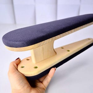 May include: A wooden sleeve board with a navy blue padded top and bottom. The board has a light wood base and a navy blue padded top. The board is held by a hand.