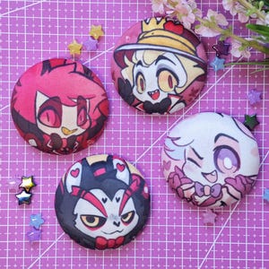 Puede incluir: Cuatro pines redondos y coloridos con personajes. Cada pin presenta un personaje de dibujos animados diferente con expresiones faciales y atuendos detallados. Los pines están colocados sobre una superficie de cuadrícula púrpura con decoraciones en forma de estrella.