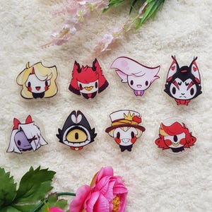 May include: Eight acrylic charms featuring cartoon characters from the animated series "Hazbin Hotel". The characters include: Angel Dust, Alastor, Charlie, Vaggie, Sir Pentious, Lucifer, and two versions of the character,  "Radio Demon".