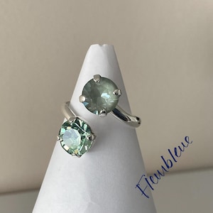 May include: A silver ring with two green gemstones. The ring is designed to be worn on the knuckle of the finger.