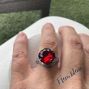 May include: A silver ring with an ornate design features a large, round, red gemstone.
