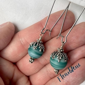 May include: A pair of silver dangle earrings with green and white striped glass beads. The beads are accented with silver filigree.