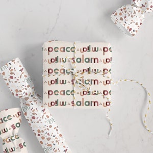 May include: Three gift wrapped boxes with a terrazzo pattern and the words "peace" and "salam" in Arabic and English. The boxes are tied with white string and a gold ribbon.