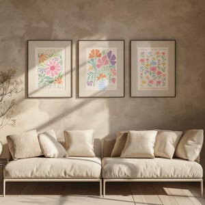 Neutral living room with a sofa and soft-toned decor, displaying a gallery wall of framed floral artworks. The main design features pastel flowers and text reading “NEVER BE SO KIND YOU FORGET TO BE CLEVER” and “NEVER BE SO CLEVER YOU FORGET TO BE KIND,” adding a calm, positive message and soft color palette that works well in modern, cozy, or minimalist spaces