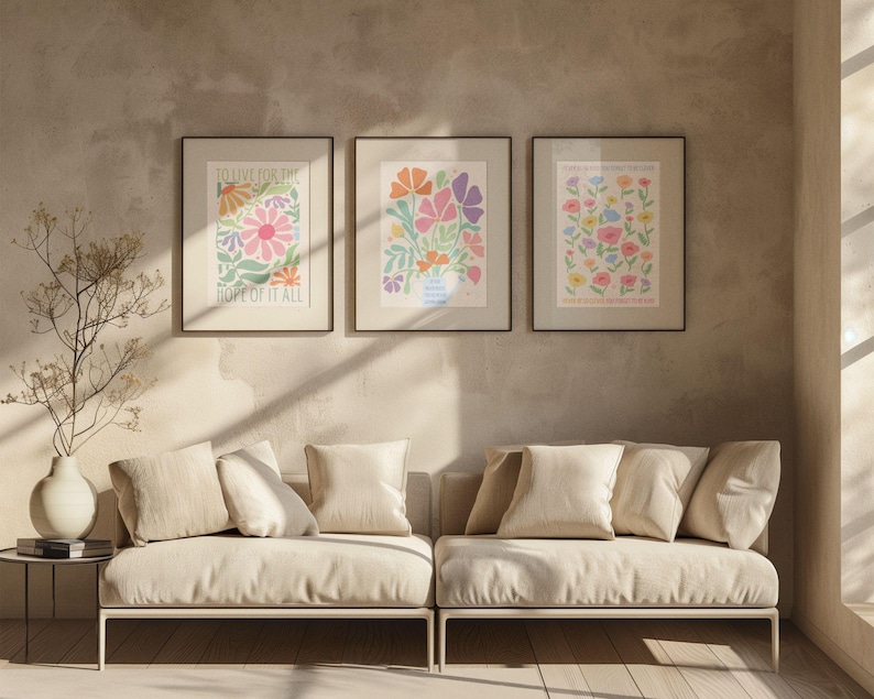 Neutral living room with a sofa and soft-toned decor, displaying a gallery wall of framed floral artworks. The main design features pastel flowers and text reading “NEVER BE SO KIND YOU FORGET TO BE CLEVER” and “NEVER BE SO CLEVER YOU FORGET TO BE KIND,” adding a calm, positive message and soft color palette that works well in modern, cozy, or minimalist spaces