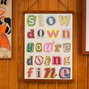 May include: A white framed poster with the words "slow down you're doing fine" in colorful, cut-out letters.