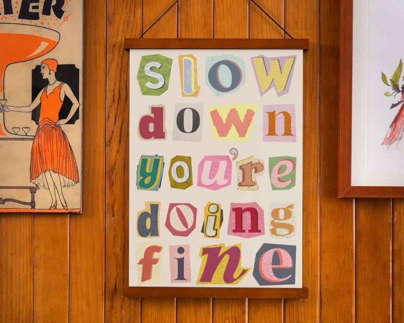May include: A white framed poster with the words "slow down you're doing fine" in colorful, cut-out letters.