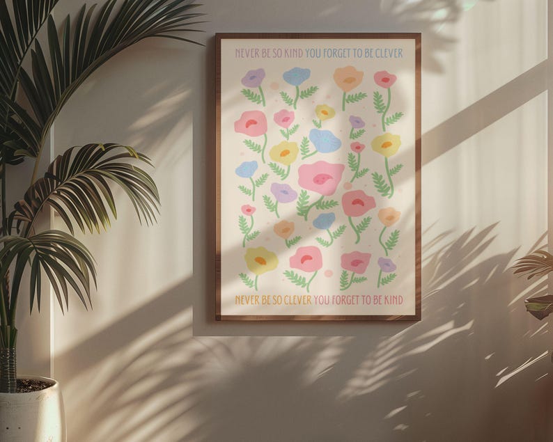 Cozy interior with warm light and minimal decor, displaying a framed floral artwork on the wall. The design features scattered pastel flowers and text reading “NEVER BE SO KIND YOU FORGET TO BE CLEVER” and “NEVER BE SO CLEVER YOU FORGET TO BE KIND,” creating a calming, uplifting piece that works well in feminine, cottagecore, or soft aesthetic spaces