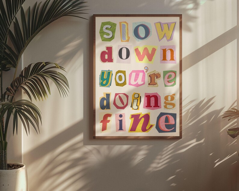 May include: A framed print with the text "slow down you're doing fine" in colorful, cut-out letters. The letters are arranged in a vertical column and are set against a white background.