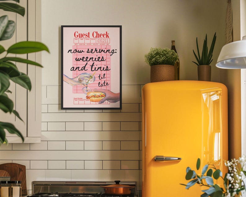 May include: A pink and white framed print with the text "Guest Check" and "now serving: weenies and tinis til late". The print features a cartoon image of a hand holding a hot dog and another hand holding a martini glass.