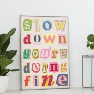 May include: A framed print with the words "slow down you're doing fine" in colorful, cut-out letters. The letters are arranged in a grid pattern on a white background.