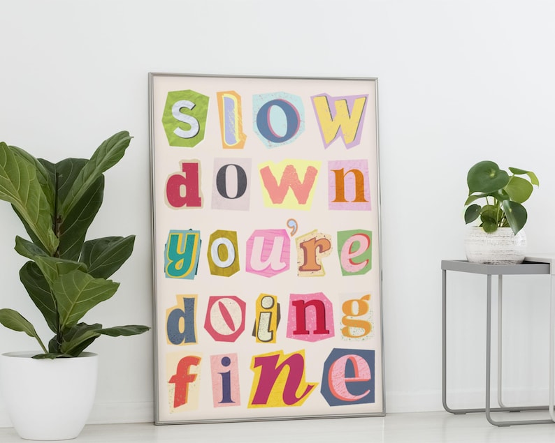 May include: A framed print with the words "slow down you're doing fine" in colorful, cut-out letters. The letters are arranged in a grid pattern on a white background.