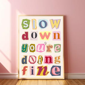 May include: A framed print with the text "slow down you're doing fine" in colorful, cut-out letters on a white background.