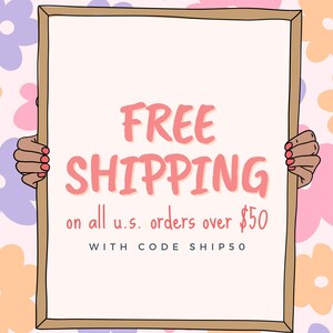 May include: A white sign with a brown frame held by two hands. The sign says "FREE SHIPPING on all u.s. orders over $50 WITH CODE SHIP50". The sign is against a pink background with colorful flowers.