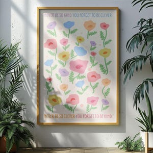 Sunlit room with leafy plants casting shadows across the wall, featuring a framed floral artwork. The design shows soft pastel flowers and green stems with text reading “NEVER BE SO KIND YOU FORGET TO BE CLEVER” and “NEVER BE SO CLEVER YOU FORGET TO BE KIND,” adding a gentle, positive message and soft color palette to modern or nature-inspired interiors