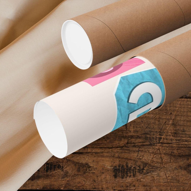 May include: Two brown cardboard tubes, one with a white cap, and another with a partially visible design in pink and blue. The tubes are on a wooden surface, with a tan paper in the background. The design on the tube appears to be a graphic.