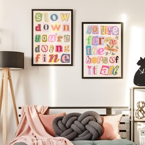 May include: Two framed prints with colorful text on a white wall. The print on the left says "Slow down you're doing fine". The print on the right says "To live for the hope of it all".
