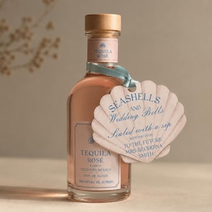 May include: A bottle of Tequila Rosé Blanco with a wooden stopper and a light blue ribbon. A seashell-shaped tag reads "Seashells and Wedding Bells, Sealed with a sip" and the date. The bottle contains 50ml.
