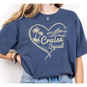 May include: Navy blue t-shirt with a heart-shaped design featuring palm trees, a cruise ship, and the text "2026 Cruise Squad" in a light beige color. The shirt is made of a soft material.
