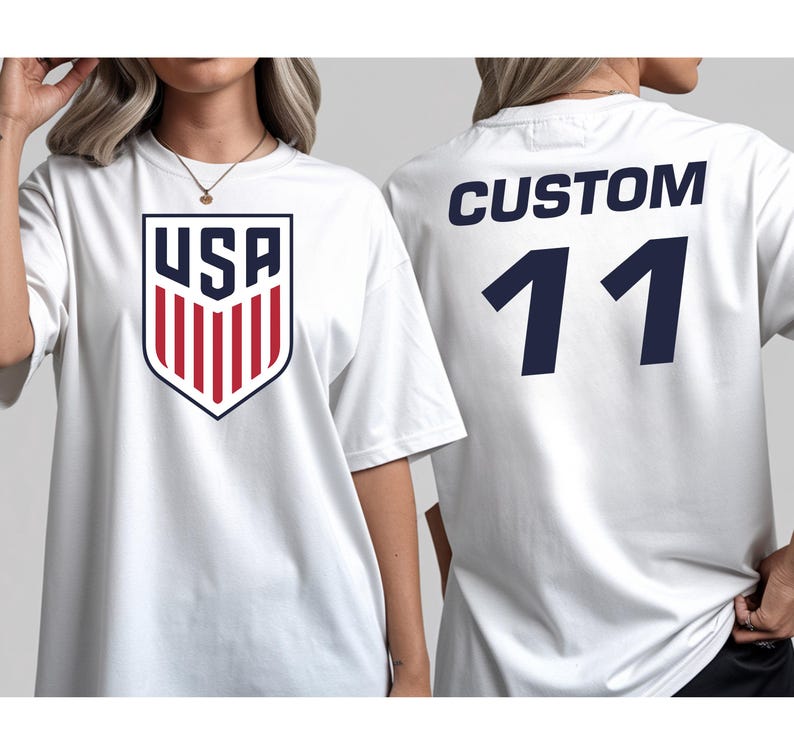 A white t-shirt with a large shield-shaped logo and the text "USA" printed on it, along with the number "11" printed below.