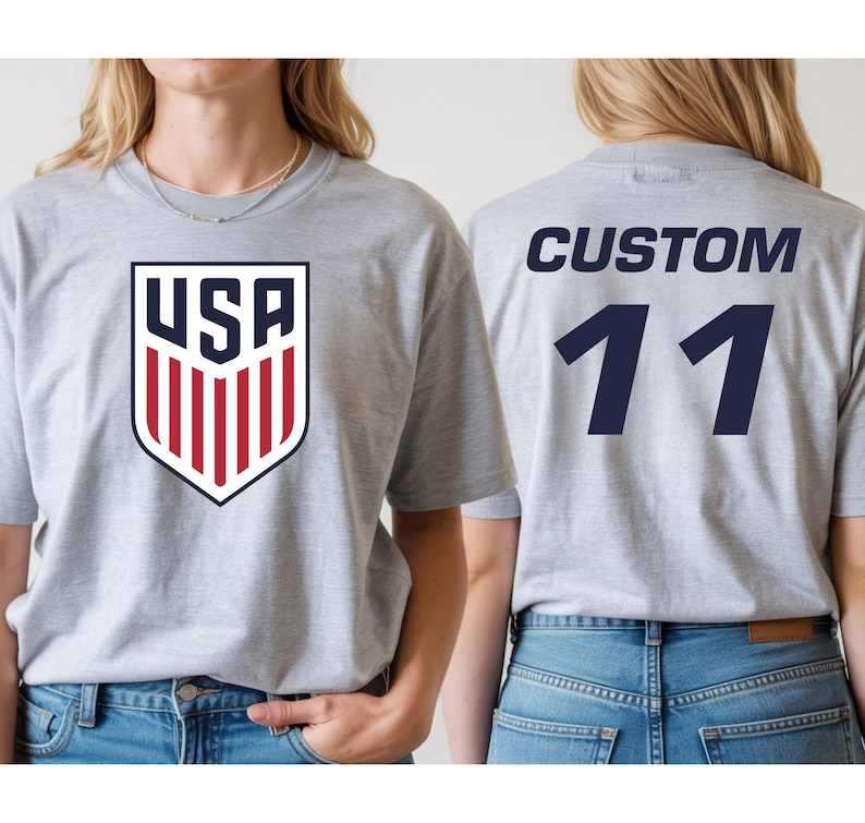 A woman wearing a grey t-shirt with a large shield-shaped logo and the text "USA" on it, as well as the number "11" on the back.