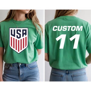 A woman wearing a green t-shirt with a large shield logo and the number 11 on the back.