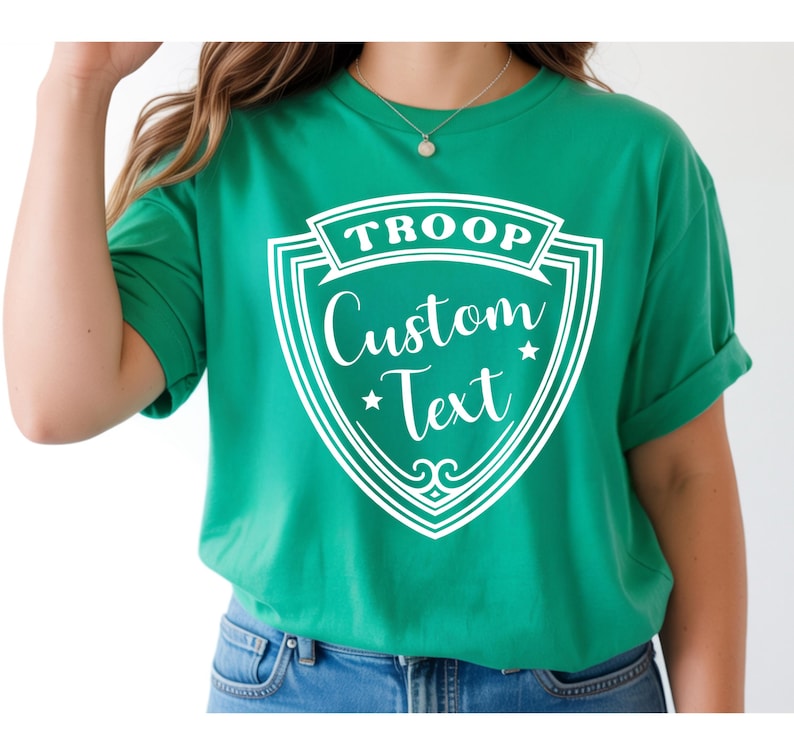 A person wearing a green T-shirt with a shield-shaped design and text printed on it.