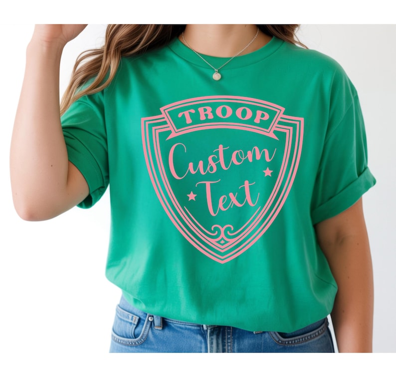 A woman wearing a green t-shirt with a pink and white shield design that says "Troop Custom Text".