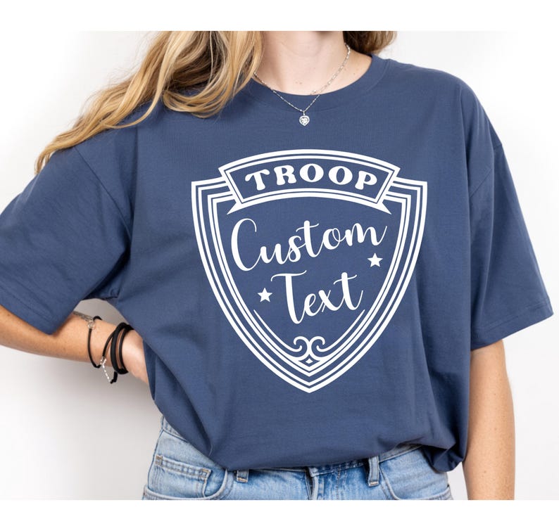 A person wearing a navy blue t-shirt with a white shield design and text printed on it.