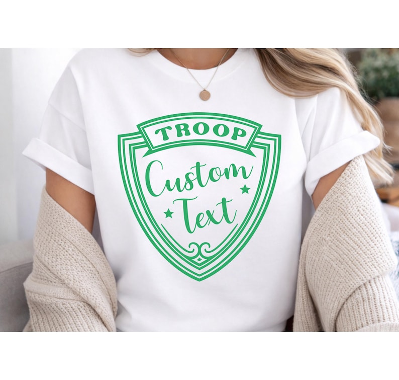 A person wearing a white T-shirt with a green shield-shaped logo that says "TROOP Custom Text".