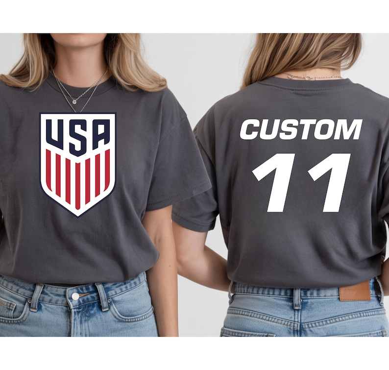 A woman wearing a grey t-shirt with a large shield-shaped logo and the text "USA" on it, and a custom number "11" on the back.